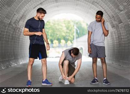 fitness, sport and healthy lifestyle concept - smiling young men or male friends with earphones training outdoors. male friends with earphones training outdoors
