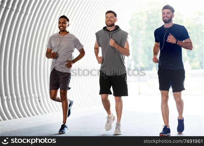 fitness, sport and healthy lifestyle concept - smiling young men or male friends with earphones running outdoors. male friends with earphones running outdoors