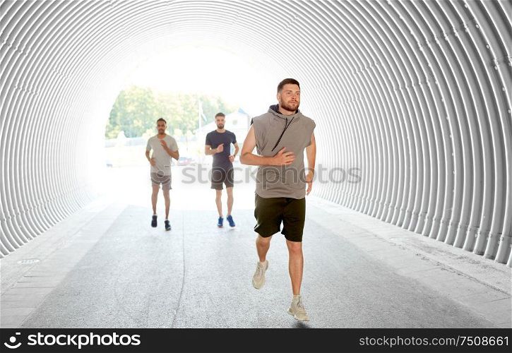 fitness, sport and healthy lifestyle concept - smiling young men or male friends running in tunnel. young men or male friends running in tunnel