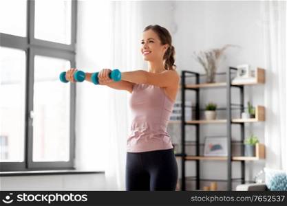 fitness, sport and healthy lifestyle concept - smiling young woman with dumbbells exercising at home. smiling young with dumbbells exercising at home