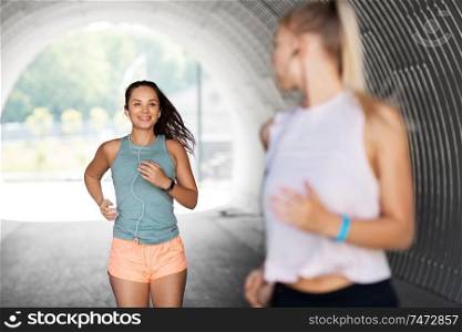 fitness, sport and healthy lifestyle concept - smiling young women or female friends with earphones running outdoors. women or female friends with earphones running