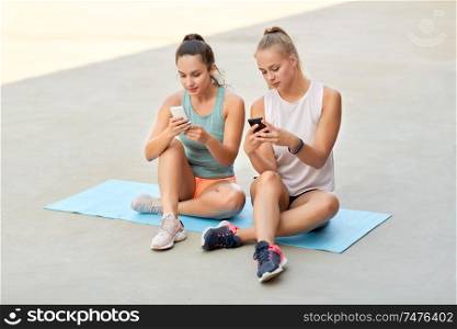 fitness, sport and healthy lifestyle concept - smiling young women or female friends with smartphones on rooftop. sporty women or friends with smartphone on rooftop