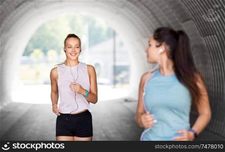 fitness, sport and healthy lifestyle concept - smiling young women or female friends with earphones running outdoors. women or female friends with earphones running