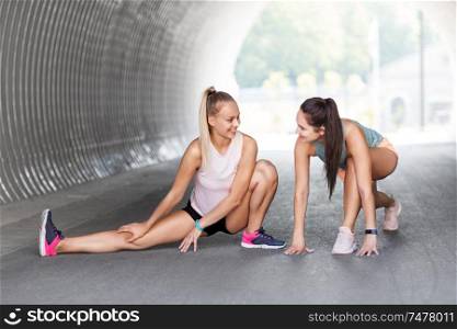 fitness, sport and healthy lifestyle concept - smiling young women or female friends with activity trackers stretching outdoors. women with fitness trackers stretching outdoors