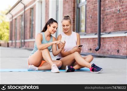 fitness, sport and healthy lifestyle concept - smiling young women or female friends with smartphone on rooftop. sporty women or friends with smartphone on rooftop