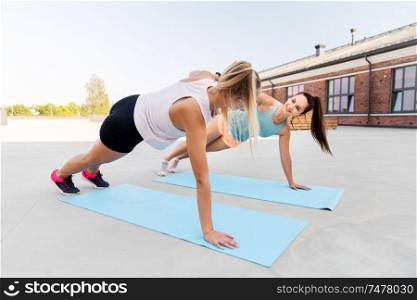 fitness, sport and healthy lifestyle concept - smiling young women or female friends making high five in side plank outdoors. women making high five in side plank on sport mats