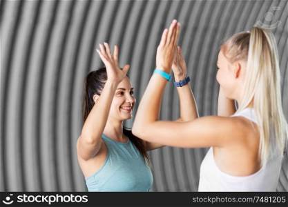fitness, sport and healthy lifestyle concept - smiling young women or female friends with activity trackers making high five outdoors. happy women with fitness trackers making high five