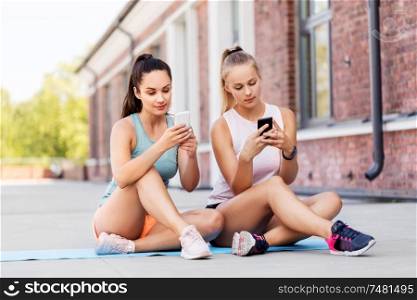 fitness, sport and healthy lifestyle concept - smiling young women or female friends with smartphone on rooftop. sporty women or friends with smartphone on rooftop