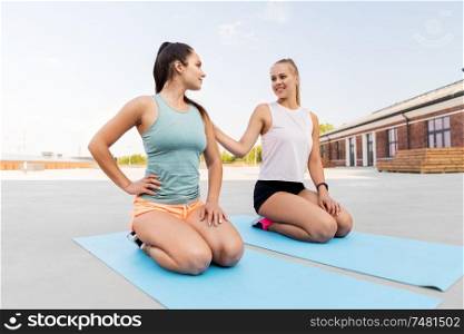 fitness, sport and healthy lifestyle concept - smiling young women or female friends sitting on exercise mats outdoors. happy women sitting on exercise mats outdoors