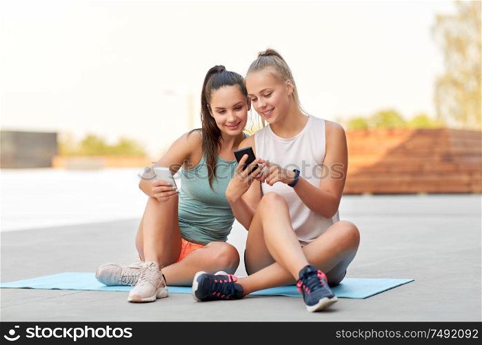 fitness, sport and healthy lifestyle concept - smiling young women or female friends with smartphones on rooftop. sporty women or friends with smartphone on rooftop
