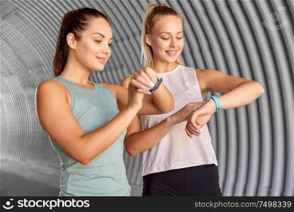 fitness, sport and healthy lifestyle concept - smiling young women or female friends looking at their activity trackers outdoors. women or female friends with fitness trackers