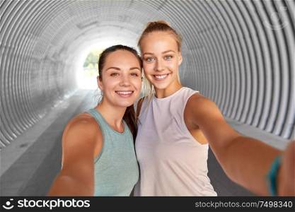 fitness, sport and healthy lifestyle concept - smiling young women or female friends taking selfie in tunnel. sporty women or friends taking selfie in tunnel