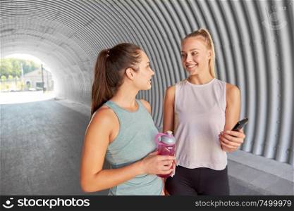 fitness, sport and healthy lifestyle concept - smiling young women or female friends with smartphone and flask. women or female friends with smartphone and flask