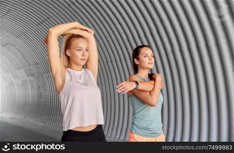 fitness, sport and healthy lifestyle concept - smiling young women or female friends with activity trackers stretching outdoors. women with fitness trackers stretching outdoors