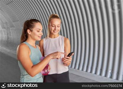 fitness, sport and healthy lifestyle concept - smiling young women or female friends with smartphone and flask. women or female friends with smartphone and flask