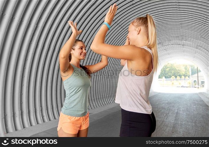 fitness, sport and healthy lifestyle concept - smiling young women or female friends with activity trackers making high five outdoors. happy women with fitness trackers making high five
