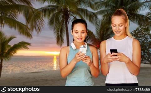 fitness, sport and healthy lifestyle concept - smiling young women or female friends with smartphones over palm trees on tropical beach on background. women or female friends with smartphones