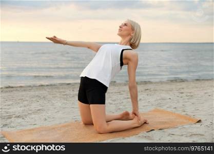 fitness, sport, and healthy lifestyle concept - woman doing yoga camel pose on beach over sunset. woman doing yoga camel pose on beach