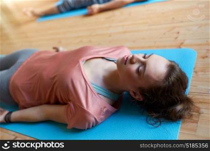 fitness, sport and healthy lifestyle concept - woman doing yoga corpse pose on mats at studio. woman with group of people doing yoga at studio