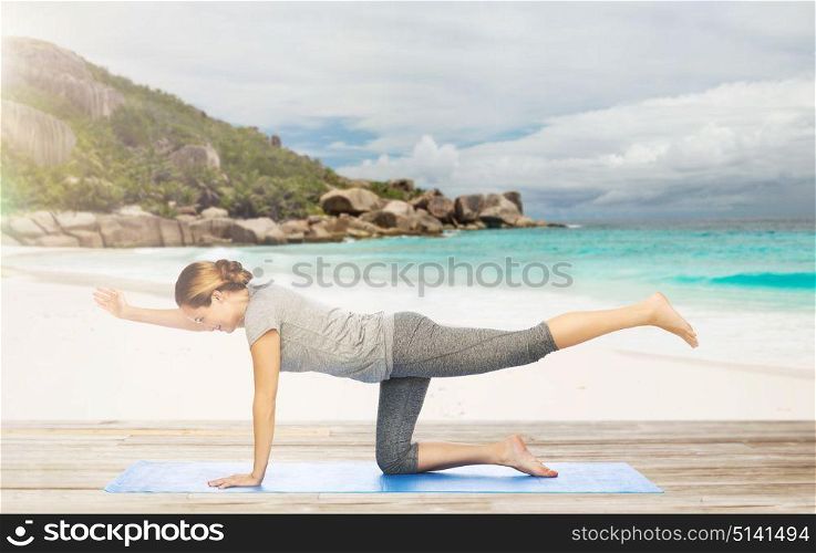 fitness, sport and healthy lifestyle concept - woman doing yoga in balancing table pose on mat over exotic tropical beach background. woman doing yoga in balancing table pose on beach