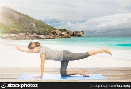 fitness, sport and healthy lifestyle concept - woman doing yoga in balancing table pose on mat over exotic tropical beach background. woman doing yoga in balancing table pose on beach