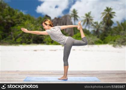 fitness, sport and healthy lifestyle concept - woman doing yoga in lord of the dance pose on mat over exotic tropical beach background. woman doing yoga lord of the dance pose on beach