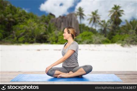 fitness, sport and healthy lifestyle concept - woman doing yoga in twist pose on mat over exotic tropical beach background. woman doing yoga in twist pose on beach
