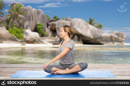 fitness, sport and healthy lifestyle concept - woman doing yoga in twist pose on mat over exotic tropical beach background. woman doing yoga in twist pose on beach