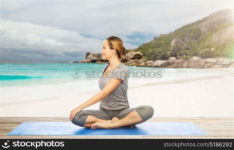 fitness, sport and healthy lifestyle concept - woman doing yoga in twist pose on mat over exotic tropical beach background. woman doing yoga in twist pose on beach