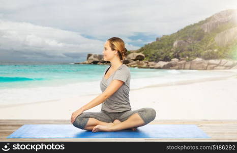 fitness, sport and healthy lifestyle concept - woman doing yoga in twist pose on mat over exotic tropical beach background. woman doing yoga in twist pose on beach