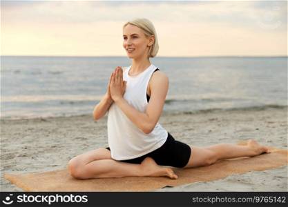 fitness, sport, and healthy lifestyle concept - woman doing yoga pigeon pose on beach over sunset. woman doing yoga pigeon pose on beach