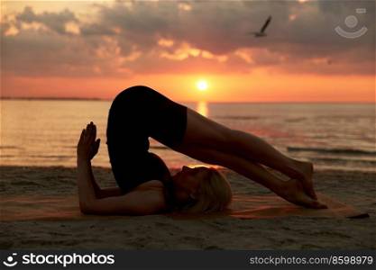 fitness, sport, and healthy lifestyle concept - woman doing yoga plow pose on beach over sunset. woman doing yoga plow pose on beach