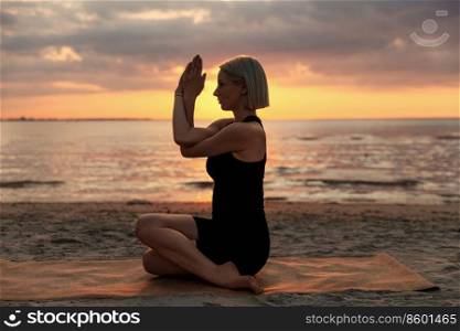 fitness, sport, and healthy lifestyle concept - woman doing yoga seated eagle pose on beach over sunset. woman doing yoga seated eagle pose on beach