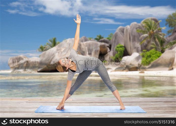 fitness, sport and healthy lifestyle concept - woman doing yoga triangle pose on mat over exotic tropical beach background. woman doing yoga triangle pose on beach