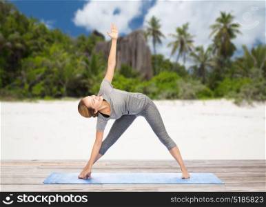 fitness, sport and healthy lifestyle concept - woman doing yoga triangle pose on mat over exotic tropical beach background. woman doing yoga triangle pose on beach