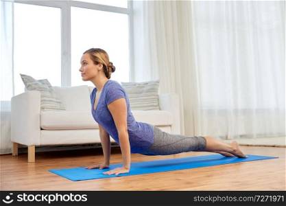 fitness, sport and healthy lifestyle concept - woman doing yoga upward-facing dog pose on mat at home. woman does upward-facing dog pose at home