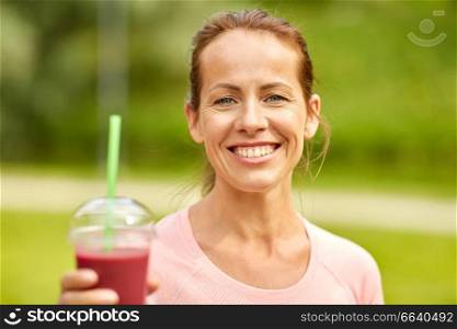 fitness, sport and healthy lifestyle concept - woman drinking takeaway smoothie or shake from plastic cup after exercising at summer park. woman drinking smoothie after exercising in park
