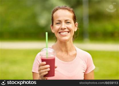 fitness, sport and healthy lifestyle concept - woman drinking takeaway smoothie or shake from plastic cup after exercising at summer park. woman drinking smoothie after exercising in park