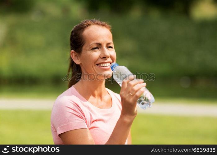 fitness, sport and healthy lifestyle concept - woman drinking water after exercising in park. woman drinking water after exercising in park