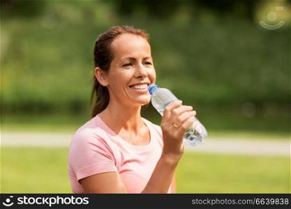 fitness, sport and healthy lifestyle concept - woman drinking water after exercising in park. woman drinking water after exercising in park