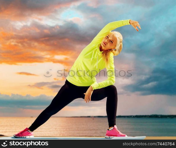 fitness, sport and healthy lifestyle concept - woman stretching on exercise mat over sea sunset background. woman stretching on exercise mat at seaside