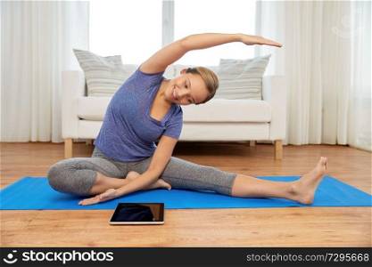 fitness, sport and healthy lifestyle concept - woman with tablet pc computer doing yoga exercises on mat at home. woman with tablet computer doing yoga at home