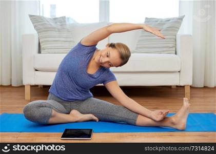 fitness, sport and healthy lifestyle concept - woman with tablet pc computer doing yoga exercises on mat at home. woman with tablet computer doing yoga at home