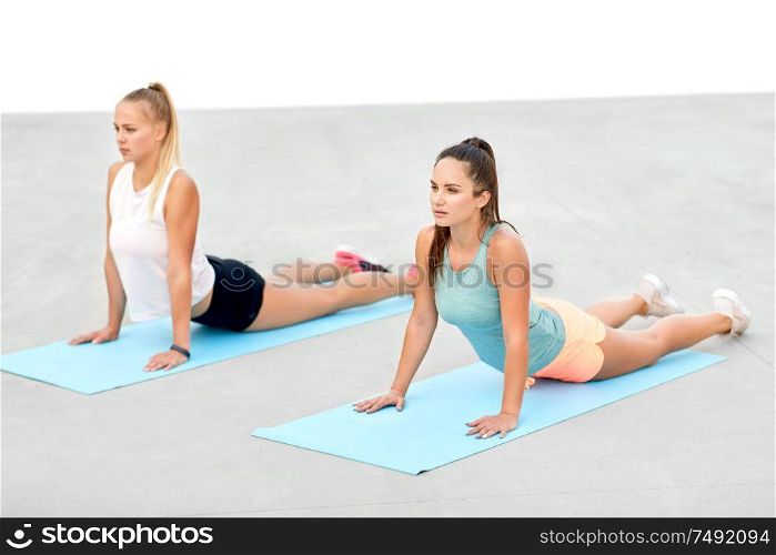 fitness, sport, and healthy lifestyle concept - women training or doing yoga on exercise mats outdoors. women doing sports on exercise mats outdoors