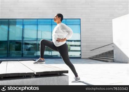 fitness, sport and healthy lifestyle concept - young african american woman stretching leg on bench outdoors. african american woman doing sports outdoors