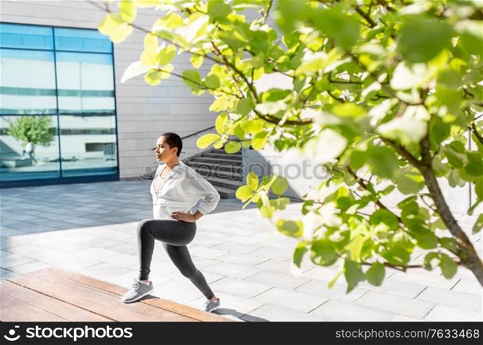 fitness, sport and healthy lifestyle concept - young african american woman stretching leg on bench outdoors. african american woman doing sports outdoors