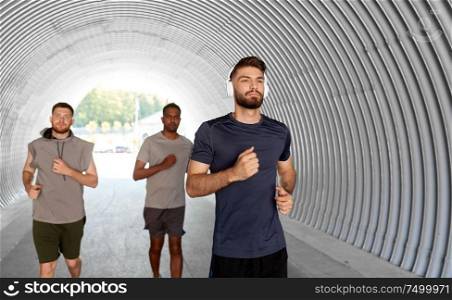 fitness, sport and healthy lifestyle concept - young men or male friends with headphones running outdoors. male friends with headphones running outdoors