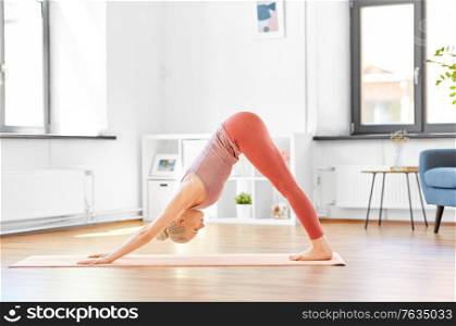 fitness, sport and healthy lifestyle concept - young woman doing yoga downward-facing dog pose on mat at home. woman does downward-facing dog yoga pose at home
