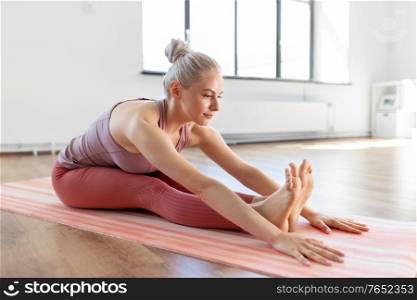 fitness, sport and healthy lifestyle concept - young woman doing yoga exercises and stretching legs on mat at home. young woman doing yoga exercise at home