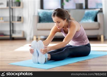 fitness, sport and healthy lifestyle concept - young woman doing yoga exercises and stretching legs on mat at home. young woman doing yoga exercise at home